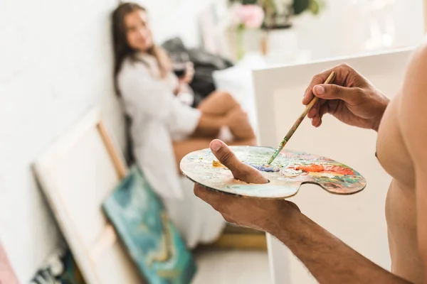 Abgeschnittene Ansicht eines hemdlosen Mannes, der Freundin mit Pinsel zeichnet, während Mädchen mit Wein im Bett sitzen — Stockfoto