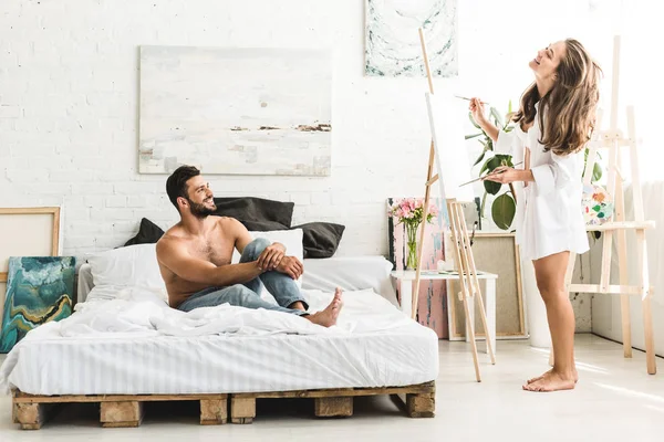 Volle Länge Ansicht von sexy Mädchen in weißer Unterwäsche Zeichnung Mann, während Kerl im Bett sitzt — Stockfoto