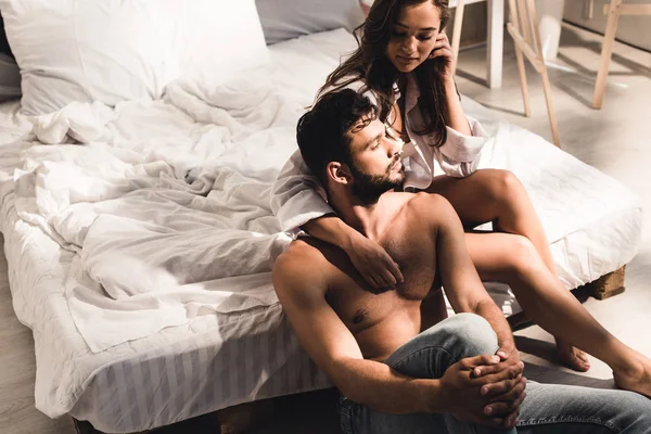 Shirtless man sitting near bed while girl sitting in bed and looking at guy — Stock Photo