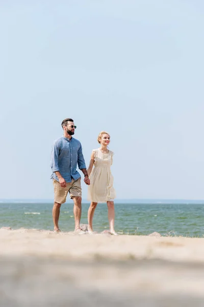 Вибірковий фокус дорослої пари, що йде вздовж пляжу і тримає руки — стокове фото