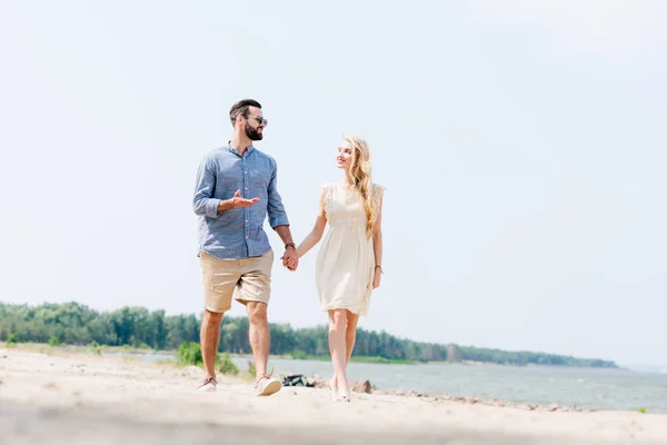 Pareja adulta caminando por la playa, hablando y tomándose de la mano - foto de stock