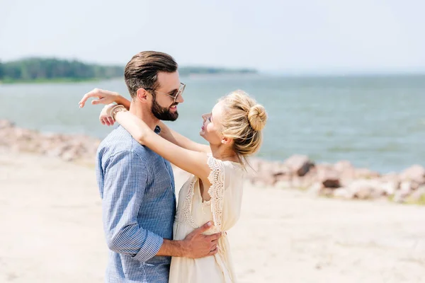 Mujer rubia feliz abrazando sonriente novio barbudo en la playa - foto de stock