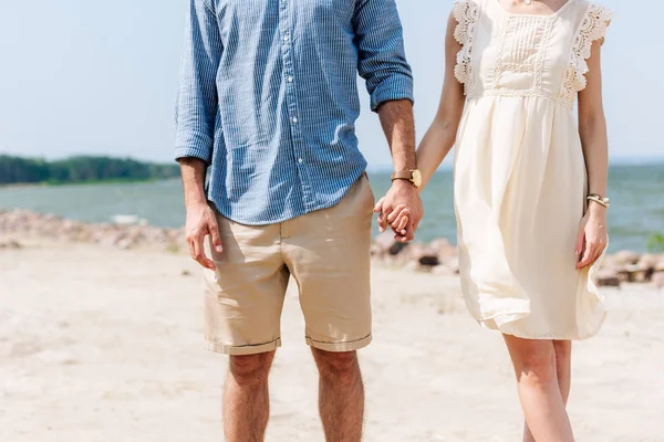 Cropped view of couple holding hands at beach — Stock Photo