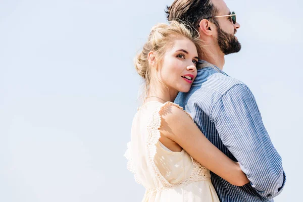 Young beautiful blonde woman hugging bearded boyfriend with clear sky on background — Stock Photo