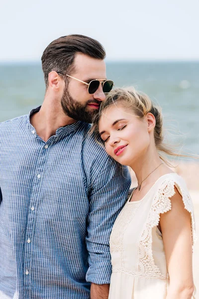 Chica rubia con los ojos cerrados apoyándose en el hombro novio mientras el hombre mira hacia la playa - foto de stock