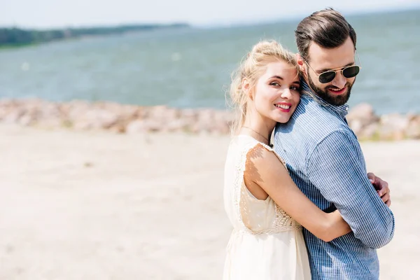 Heureuse blonde femme étreignant barbu sourire copain à la plage — Photo de stock