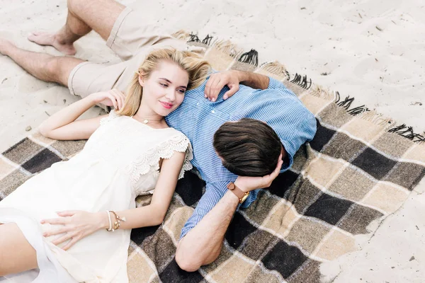 Young couple lying together on checkered blanket at sandy beach — Stock Photo