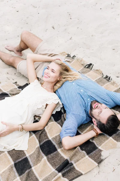 Feliz casal deitado juntos em cobertor xadrez na praia de areia — Fotografia de Stock