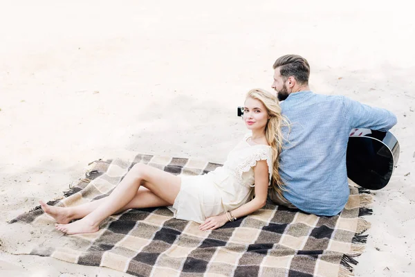 Jeune blonde pieds nus femme appuyé sur copain avec guitare acoustique à la plage — Photo de stock