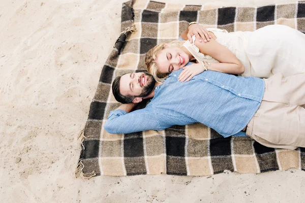 Happy couple lying together on plaid blanket at sandy beach — Stock Photo