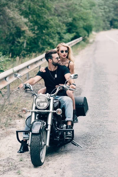 Young couple of bikers on black motorcycle on road near green forest — Stock Photo