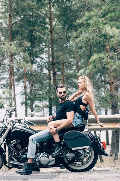 Вид збоку Sexy пара байкерів на чорному мотоциклі на дорозі біля зеленого лісу — стокове фото