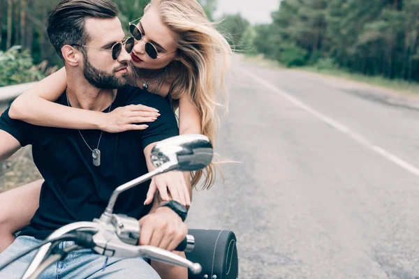 Jovem casal de motociclistas abraçando na motocicleta preta na estrada perto da floresta verde — Fotografia de Stock