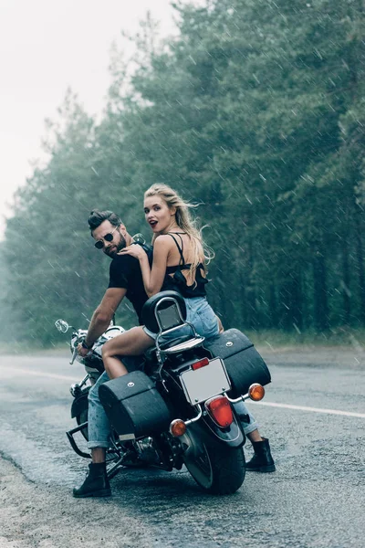 Jeune couple de motards à moto noire près de la forêt verte par temps orageux — Photo de stock