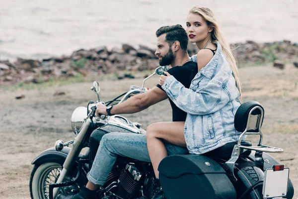 Couple of bikers sitting on black motorcycle at beach near river — Stock Photo