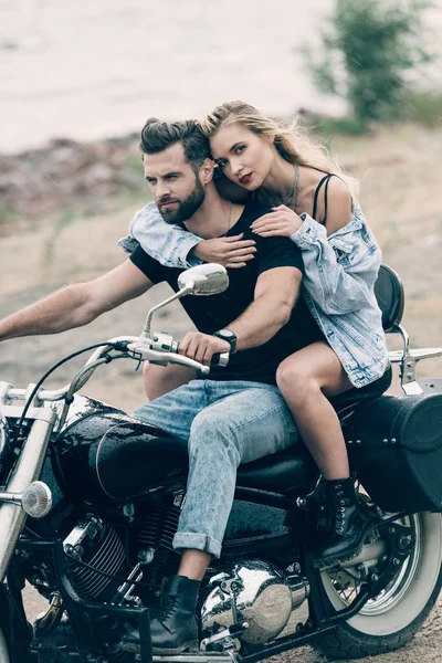 Joven pareja de ciclistas abrazándose en negro motocicleta en la playa de arena - foto de stock