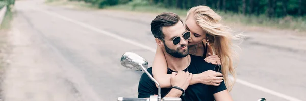 Young couple of bikers closely embracing on black motorcycle, panoramic shot — Stock Photo