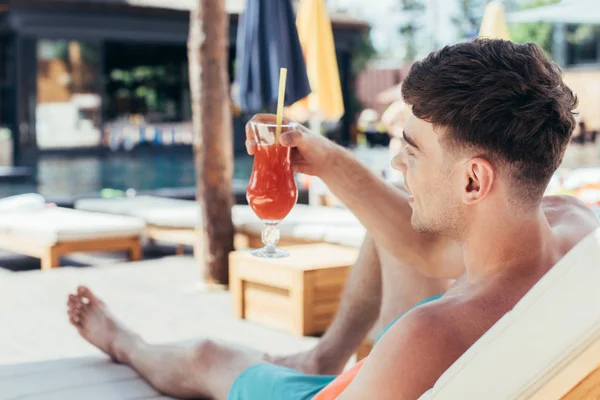 Вибірковий фокус молодого чоловіка, який розслабляється на шезлонгу зі склянкою освіжаючого напою — стокове фото