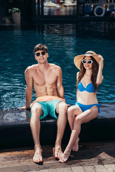 Щаслива молода пара посміхається на камеру, сидячи біля басейну — стокове фото