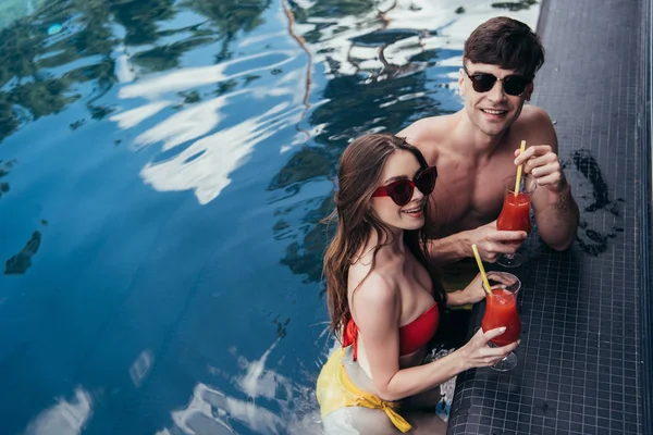 Alegre pareja joven sosteniendo vasos de bebida refrescante y sonriendo a la cámara - foto de stock