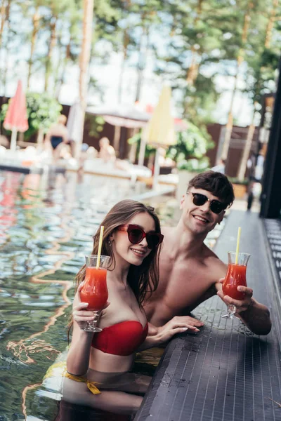 Щаслива молода пара в сонцезахисних окулярах тримає окуляри освіжаючого напою і посміхається на камеру — стокове фото