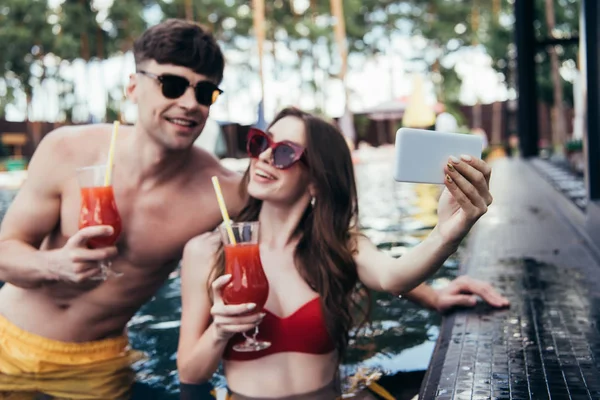 Jovem alegre tomando selfie com namorado enquanto relaxa na piscina juntos — Fotografia de Stock