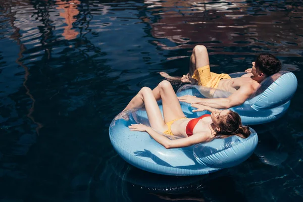 Jeune couple bronzer tout en flottant sur des anneaux de natation dans la piscine — Photo de stock