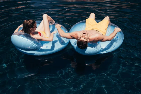 Young couple sunbathing while relaxing on swim rings in swimming pool — Stock Photo