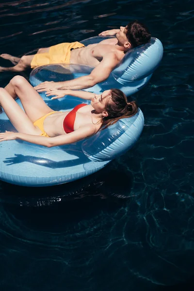 Jovem casal banhos de sol enquanto flutuava em anéis de natação na piscina — Fotografia de Stock