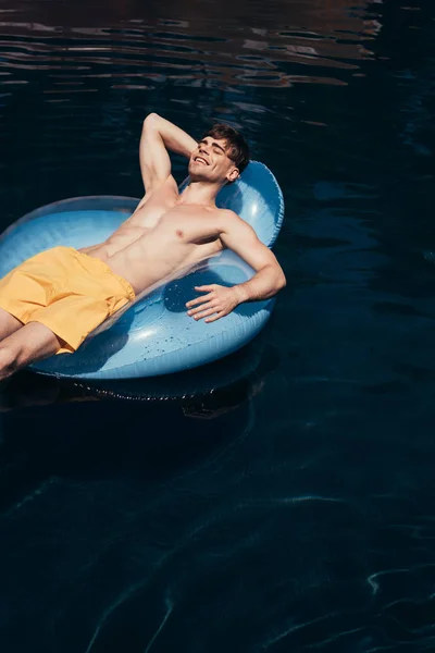 Happy handsome in swimsuit sunbathing on swim ring in swimming pool — Stock Photo