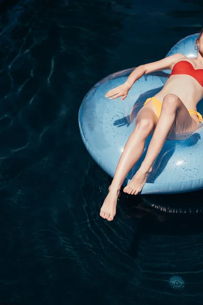 Vista cortada da jovem mulher em maiô tomando banho de sol no anel de natação na piscina — Fotografia de Stock