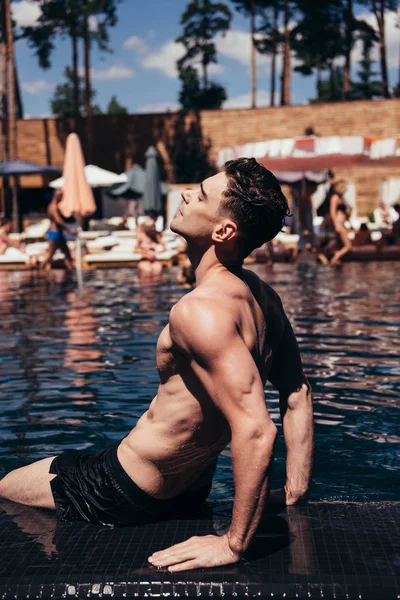 Beau jeune homme bronzer sur le bord de la piscine avec les yeux fermés — Photo de stock