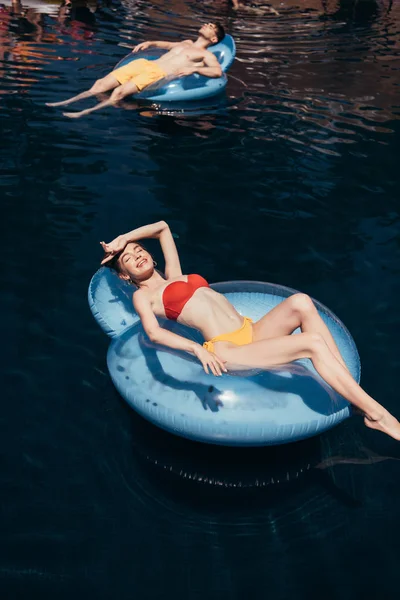 Happy young couple floating and sunbathing on swim rings in swimming pool — Stock Photo