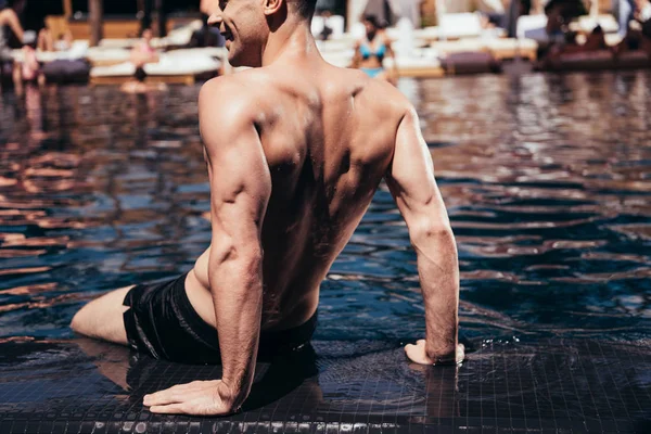 Uomo bello sorridente seduto e prendere il sole a bordo piscina e guardando altrove — Foto stock