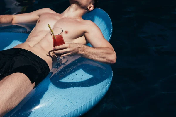 Cropped view of young man sunbathing on swim ring in swimming pool with glass of refreshing drink — Stock Photo