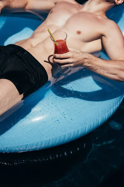 Vue partielle du jeune homme se relaxant sur l'anneau de natation dans la piscine avec verre de boisson rafraîchissante — Photo de stock