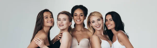 Prise de vue panoramique de cinq filles multiethniques souriant et regardant la caméra isolée sur gris — Photo de stock
