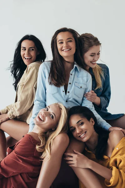 Vista frontal de cinco feministas multiétnicas atraentes sorridentes em camisas coloridas abraçando e olhando para a câmera isolada em cinza — Fotografia de Stock