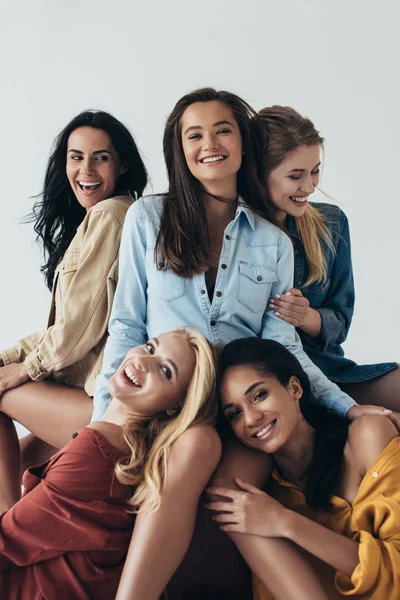 Front view of five smiling attractive multiethnic feminists in colorful shirts embracing and looking at camera isolated on grey — Stock Photo