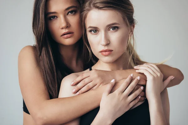 Dos atractivas feministas en ropa interior abrazándose aisladas en gris - foto de stock