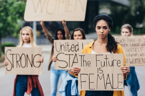 Feminista afroamericana seria sosteniendo pancarta con inscripción el futuro es femenino cerca de las mujeres en la calle - foto de stock