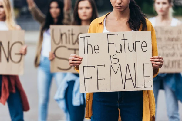 Vista recortada de niña sosteniendo pancarta con inscripción el futuro es femenino cerca de feministas en la calle - foto de stock