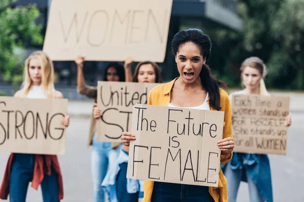 Vista frontal de gritando feminista afroamericana sosteniendo pancarta con inscripción el futuro es femenino en la calle — Stock Photo