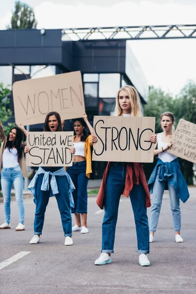 Ganzkörperansicht von Frau mit Plakat mit starkem Wort in der Nähe von Feministinnen auf der Straße — Stockfoto