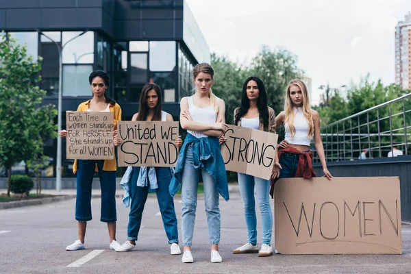 Visão de comprimento total de feministas multiétnicas segurando cartazes com slogans na rua — Fotografia de Stock
