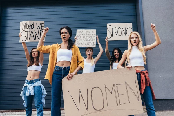 Five multiethnic feminists holding placards with slogans and screaming on street — Stock Photo