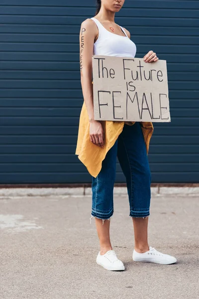 Vista recortada de feminista con palabra perfecta en el brazo sosteniendo pancarta con inscripción el futuro es femenino - foto de stock