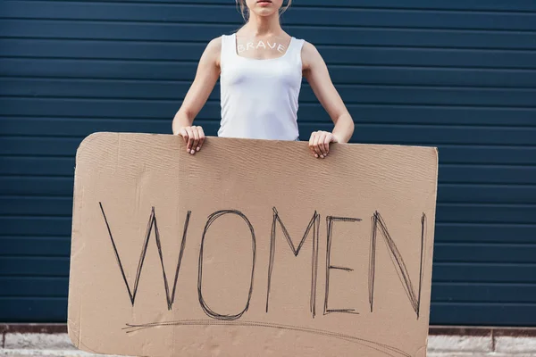 Vista recortada de feminista con palabra valiente en el cuerpo sosteniendo pancarta con mujeres inscripción en la calle - foto de stock