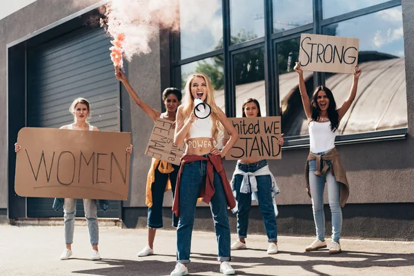 Piena lunghezza di urla femministe multietniche con altoparlanti che tengono cartelli con slogan sulla strada — Stock Photo