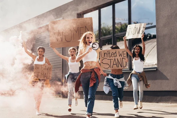 Visão de comprimento total de feministas gritando com alto-falante segurando cartazes com slogans e correndo na rua — Fotografia de Stock